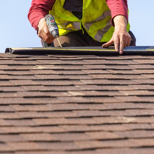 Close up photo of professional worker with electric drill repairing a shingle roof